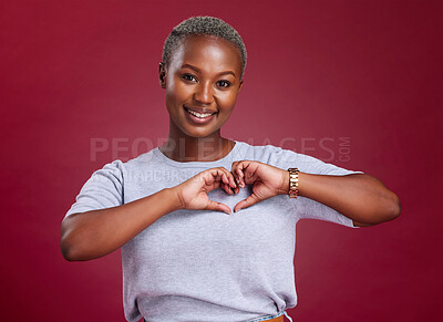 Buy stock photo Hands, heart and love with a model black woman in studio on a red background to promote health or wellness. Portrait, smile and hand sign with a young female posing to endorse romance or cardio