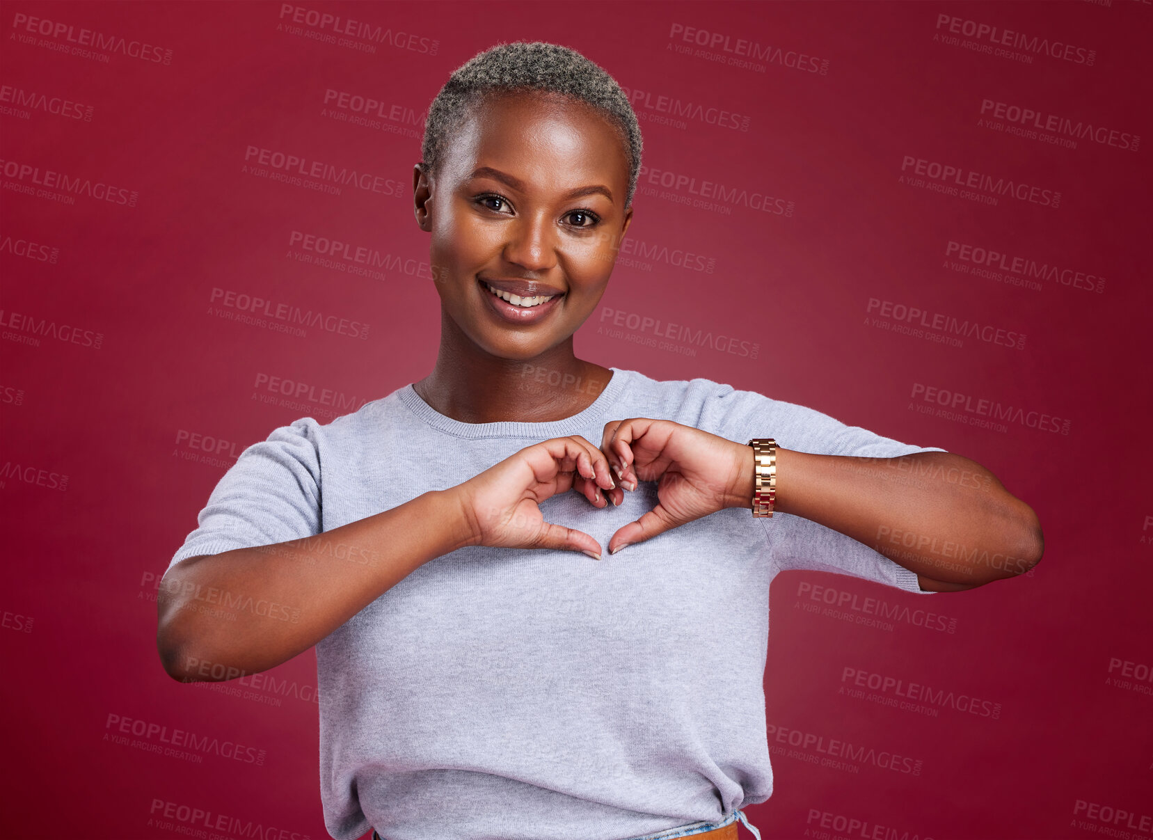 Buy stock photo Hands, heart and love with a model black woman in studio on a red background to promote health or wellness. Portrait, smile and hand sign with a young female posing to endorse romance or cardio