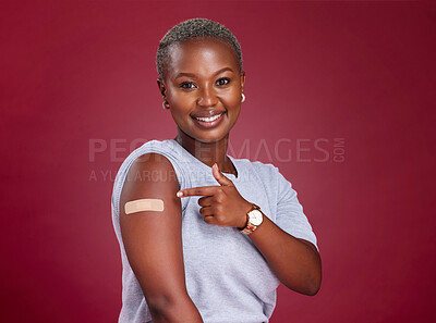 Buy stock photo Black woman, pointing and covid plaster on studio red background for healthcare wellness, medical life insurance or security. Portrait, smile and happy model with covid 19 band aid in vaccine support