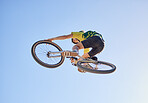 Bicycle, cyclist man and jump of adrenaline junkie from below riding in a competition with copyspace. Extreme sport, bicycle and cycling man stunt while on bike against a blue sky background 
