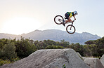 Mountain bike, jump and man doing extreme stunt while training or riding in competition. Bicycle, sports and athlete or cyclist practicing skill for fitness, contest or tournament in nature by a rock