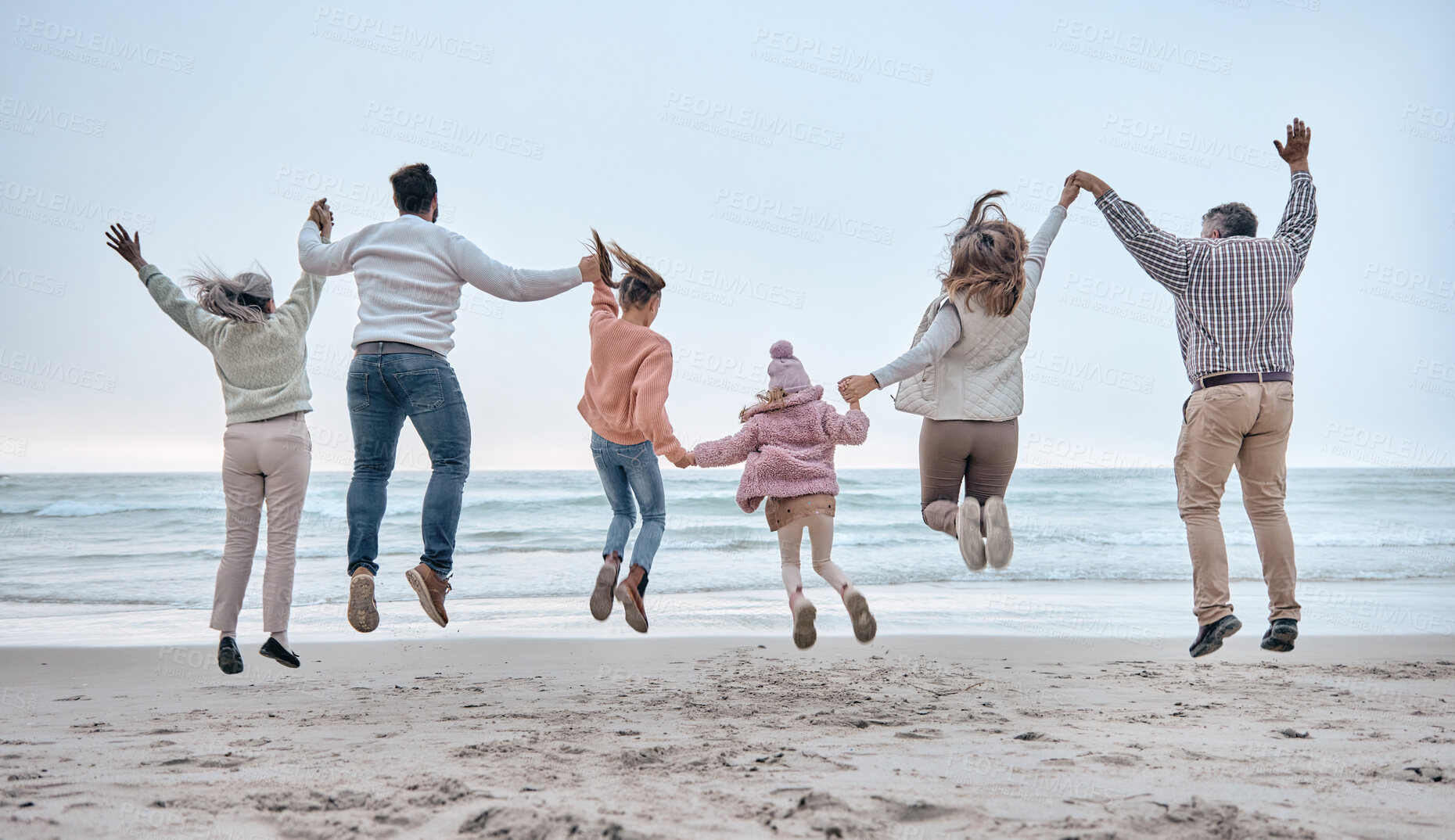 Buy stock photo Family at the beach, adventure and jump, generations love and care while holding hands and fun by the ocean. Big family travel, parents with grandparents and children together and freedom at sea.