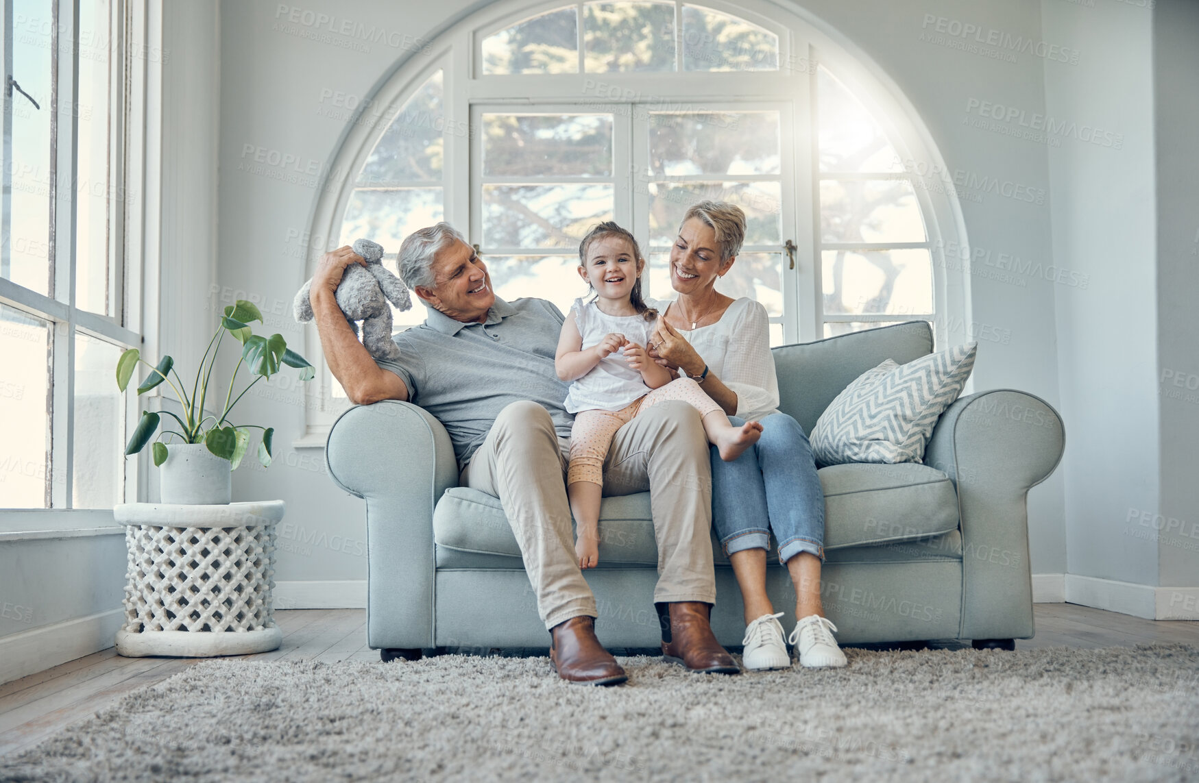Buy stock photo Happy, relax and grandparents with a child on sofa in the living room at family home. Happiness, grandmother, grandfather and girl kid sitting on couch together while playing, bonding and relaxing.