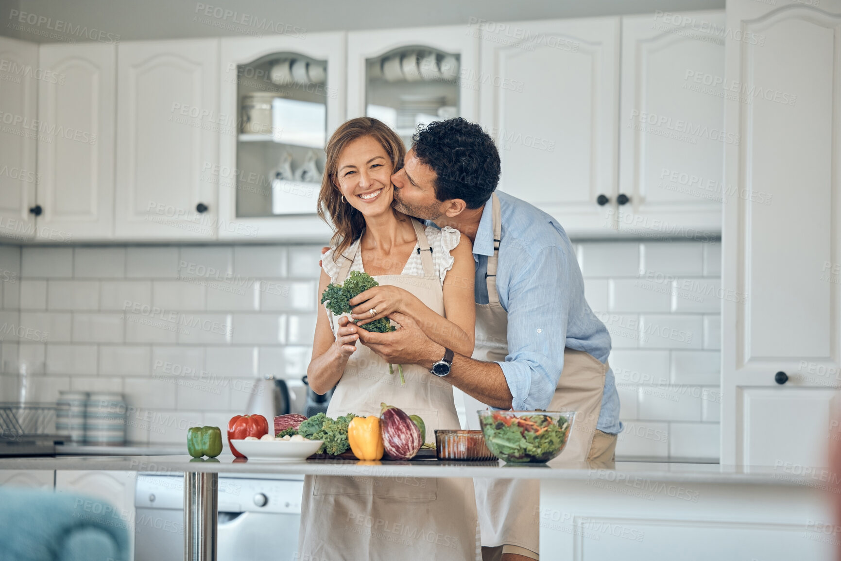 Buy stock photo Food, love and elderly couple in kitchen, kiss and hug while prepare meal, bond and smile in their home. Love, cooking and happy seniors in romantic moment while preparing a healthy salad together 
