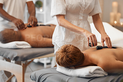 Buy stock photo Hot stone massage, black couple and relax spa in skincare wellness, healthcare or stress management in hotel salon or resort. Woman, man and massage therapist with luxury rock therapy on love retreat