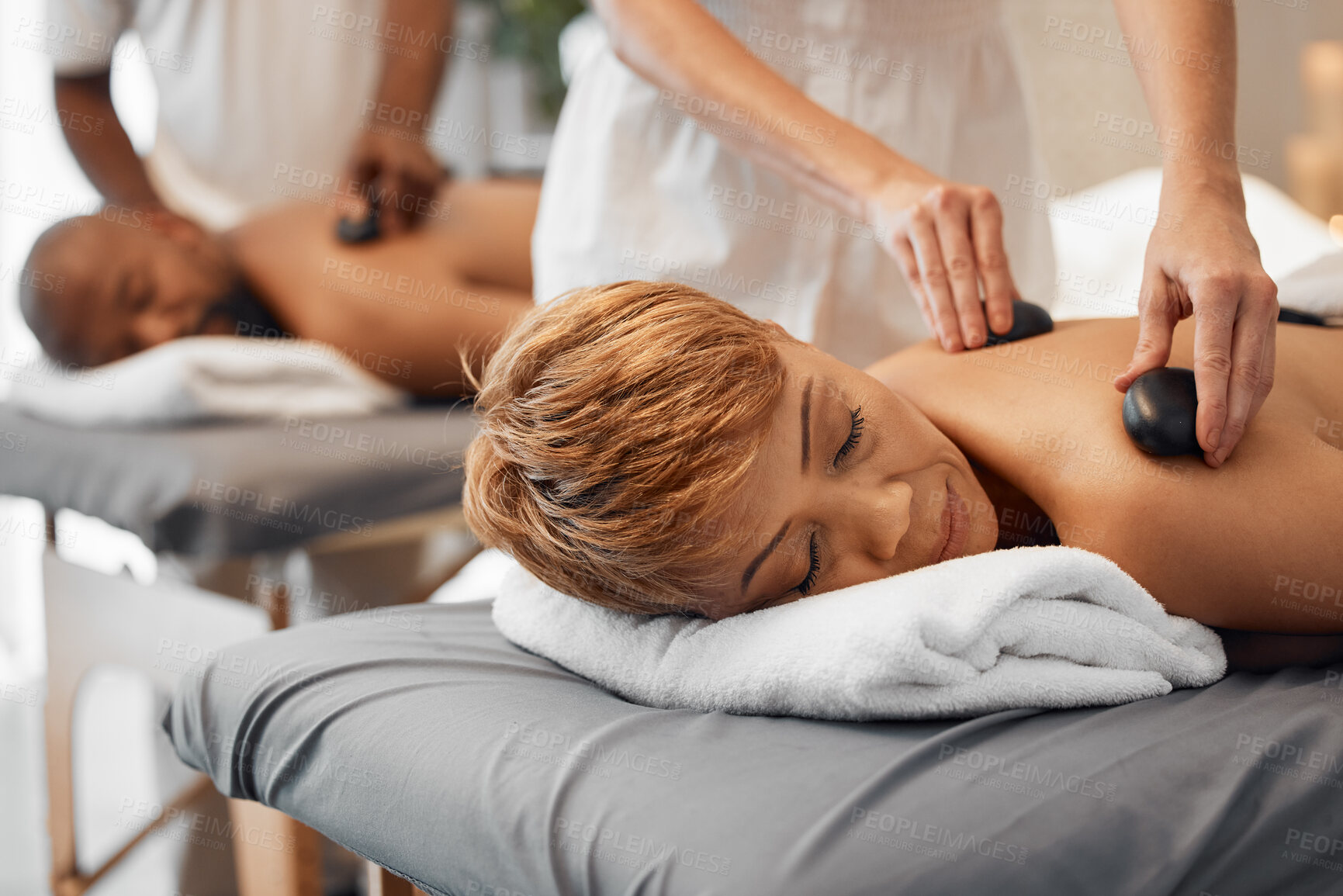 Buy stock photo Spa, couple and massage for health and wellness while on bed for hot stone or rock therapy on back for zen, peace and relax. Man and woman customer in beauty salon for physical therapy and self care