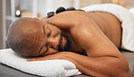 Black man, spa bed hot stone massage and relax body, treatment and luxury physical therapy for health, stress and wellness. Zen man, rest salon and rock for healthcare, recovery or skincare on back
