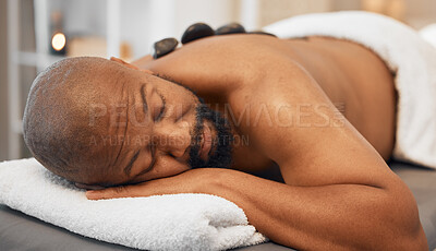 Buy stock photo Black man, spa bed hot stone massage and relax body, treatment and luxury physical therapy for health, calm and wellness. Zen man, rest salon and rock for healthcare, recovery or skincare on back