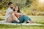 Couple relax on grass, outdoor picnic in park and love sitting on blanket in Miami garden under a tree. Romantic date in spring, woman smile at happy boyfriend or summer holiday together in sunshine