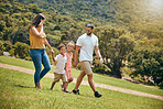 Park, family and nature walking of a mother, dad and kids outdoor in the sun on a hike. Happy mom, father and kids walk on a field with parents spending quality time together with a smile on grass