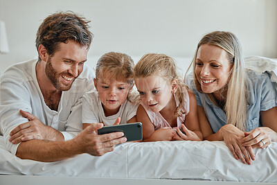 Buy stock photo Happy family with kids, phone and lying on bed in home, mother, father and girl children watching video together. Love, fun and family with dad, mom and daughters on smartphone video call in bedroom.