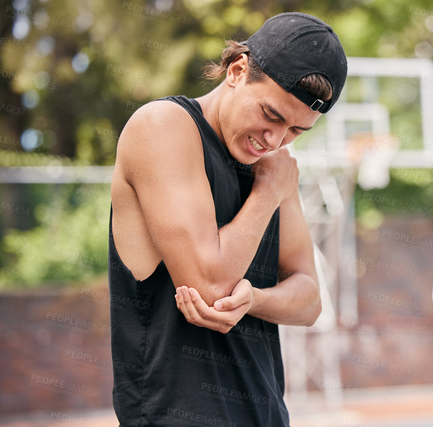 Buy stock photo Sport injury, basketball and man in pain while playing on basketball court, fitness and hurt elbow outdoor. Young athlete holding arm, sore and exercise accident, sports and training in park.