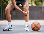 Pain, basketball and man with knee injury standing on outdoor court, holding leg. Sports, fitness and athlete with joint pain, injured and hurt in training, workout and game on basketball court