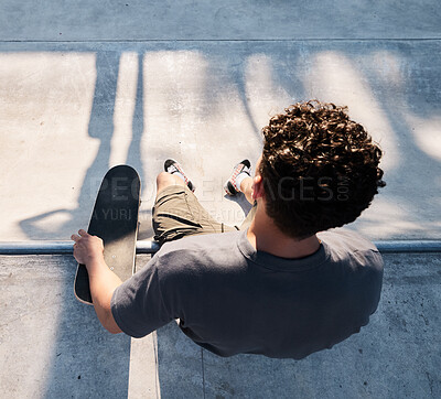 Top view of skater, man and skateboard in city, street or outdoors. Skateboarding, sports and male sitting on ramp preparing for skating practice, exercise or fitness training and workout in town.