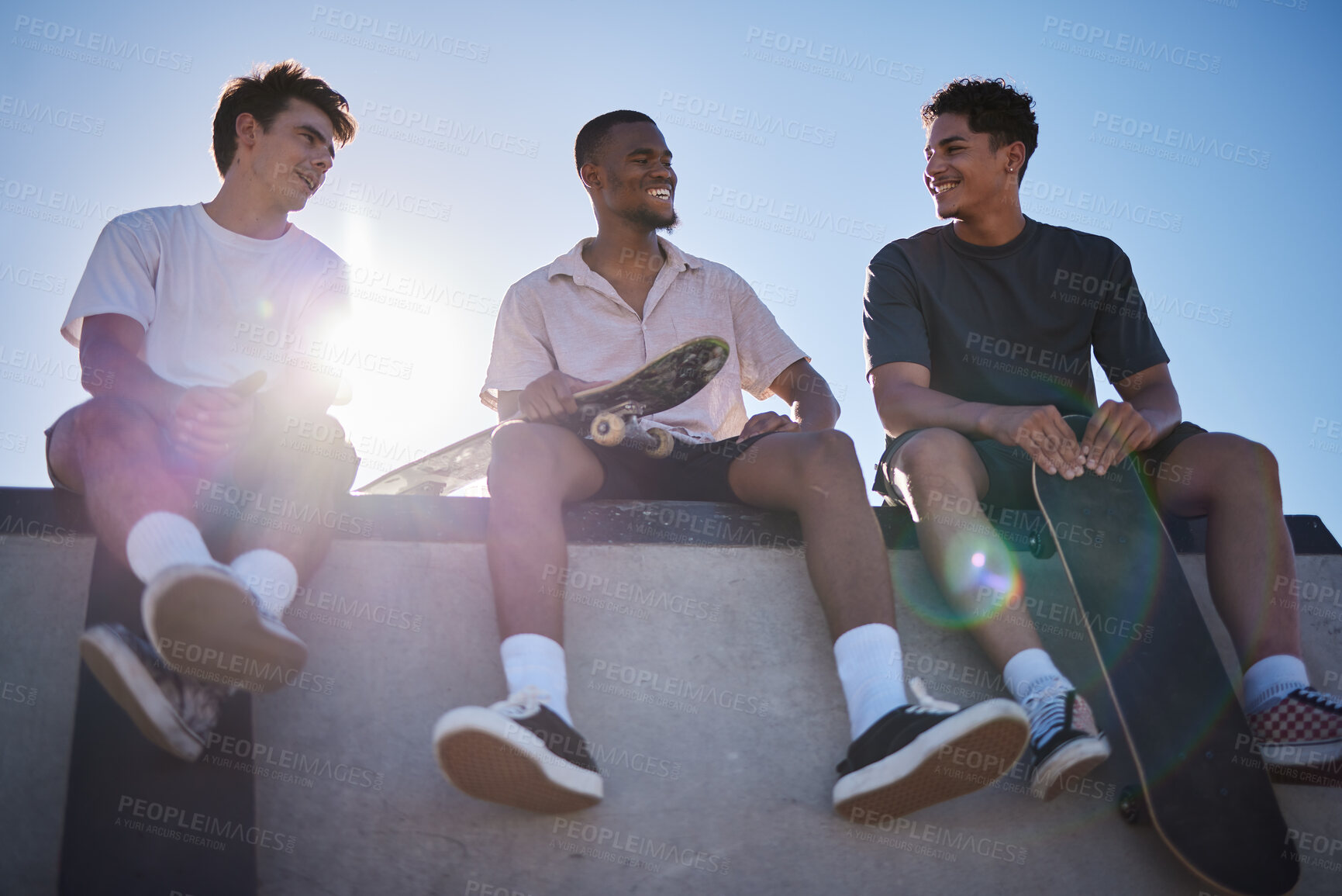 Buy stock photo Diversity, friends and men with skateboard together talking on wall in city. Happy conversation, laughing and gen z skater friendship group with street fashion bonding at skate park outdoors