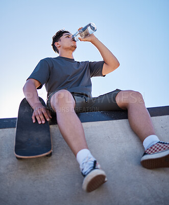Buy stock photo Skateboard, young man and drinking water bottle, relax and on break on sunny day outdoor. Male, skater and athlete hydrate, thirsty and sports for wellness, health and have fun in summer.