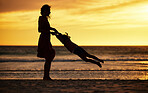 Family, silhouette and sunset at beach with mother swinging child against yellow sky with love, care and support on vacation in summer. Woman and kid by sea for travel fun, adventure and freedom
