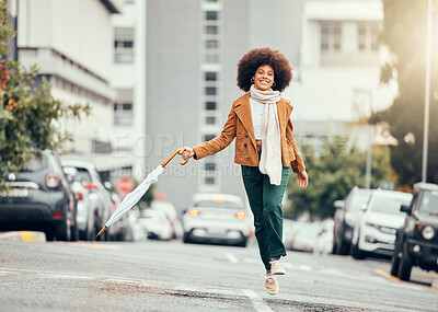 Buy stock photo Black woman, umbrella and jump on street, city or road outdoors. Happy, smile and carefree female from South Africa skipping on pavement in urban town, traveling or having fun time alone on sunny day