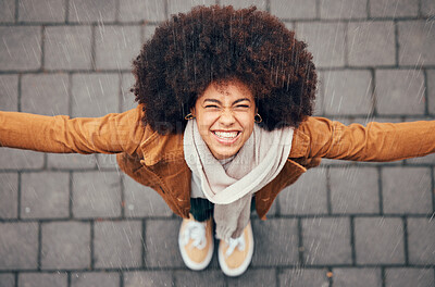 Buy stock photo Black woman, stand to feel rain and happy in city in winter with smile, afro or trendy fashion. Woman, outdoor above or happiness in drizzle, splash and face in metro, urban or town with natural hair