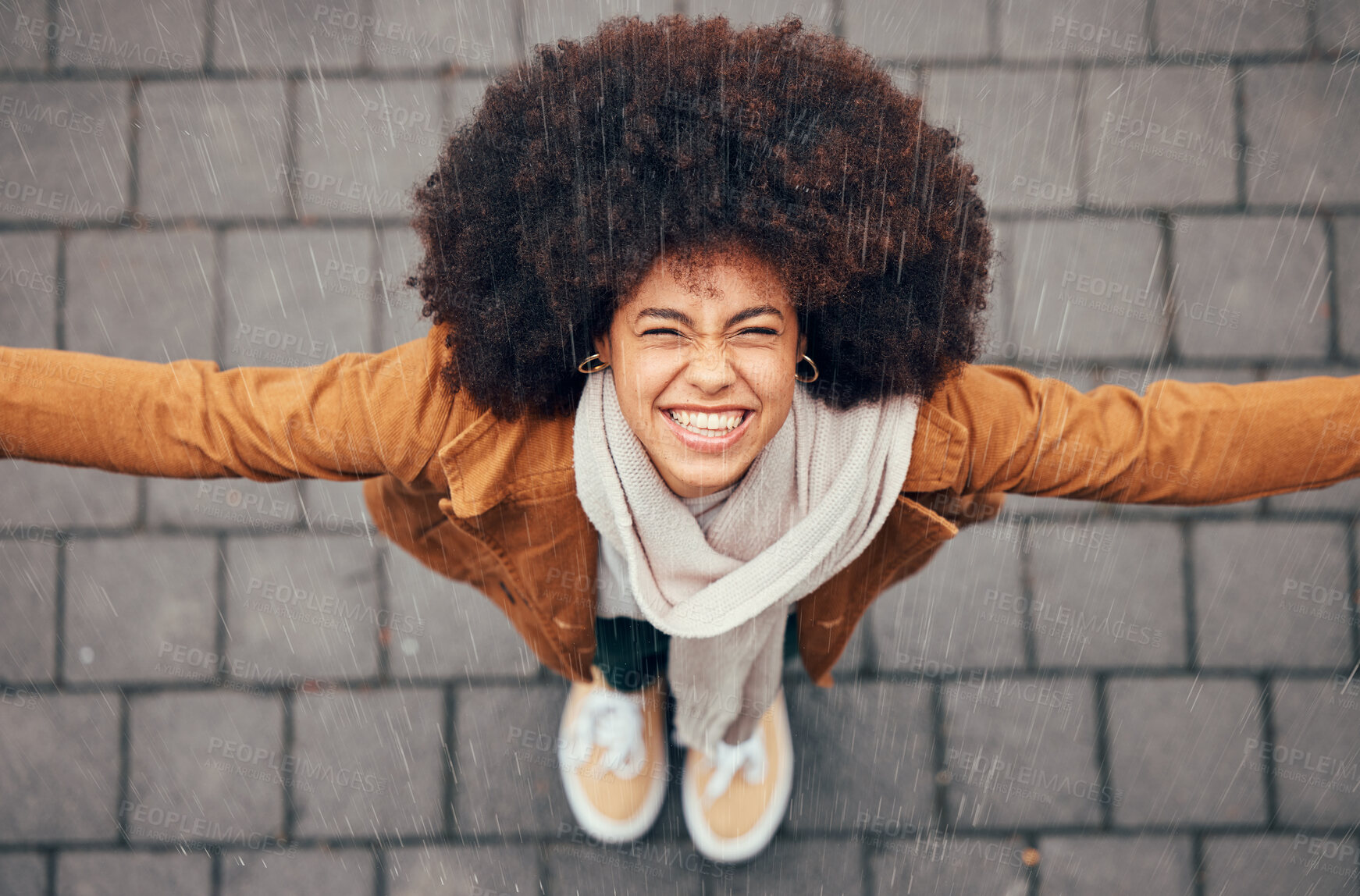 Buy stock photo Black woman, stand to feel rain and happy in city in winter with smile, afro or trendy fashion. Woman, outdoor above or happiness in drizzle, splash and face in metro, urban or town with natural hair