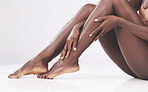 Feet, legs and skincare with a model black woman touching her soft or smooth skin in studio on a gray background. Hands, skin and luxury with a female rubbing her foot or ankle for beauty or wellness