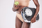 Fitness woman, scale and apple for healthy diet, exercise progress and wellness nutrition on studio background. Scales, fruit and black model measure body for weightloss training, muscle and beauty 