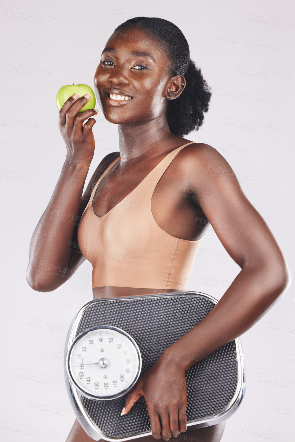 Buy stock photo Apple, scale and weightloss with a black woman in studio on a gray background to promote healthy eating or diet. Food, fruit and exercise with an attractive young female posing for natural vitamins