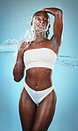 Black woman, underwear and body with water splash on blue background in studio for skincare wellness, luxury healthcare or grooming. Beauty model, wet liquid or hydration spray for hygiene cleaning