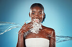 Black woman, water and splash with beauty portrait of happy skincare, shower and wellness. Hydration, fresh and clean hygiene with face model for luxury, relax and spa in a blue background in studio