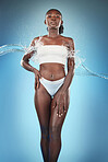 Black woman, skincare body and water splash, beauty hydration or moisturiser by studio background. Woman, skin model or bodycare for cosmetics, health or dermatology wellness by blue backdrop wall