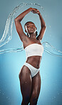 Beauty, body and water with a model black woman cleaning in studio on a blue background for hydration or wellness. Skin, splash and luxury with an attractive young female wet in a shower for hygiene