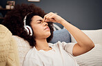 Headache, pain and woman with headphones of sofa tired, exhausted and trying to relax. Stress, fatigue and black woman listening to music at home streaming song, track and radio for stress relief