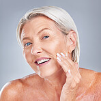 Skincare, wellness and senior woman with face for inspection, health and beauty against a grey studio background. Happy, smile and portrait of an elderly person with facial care during retirement