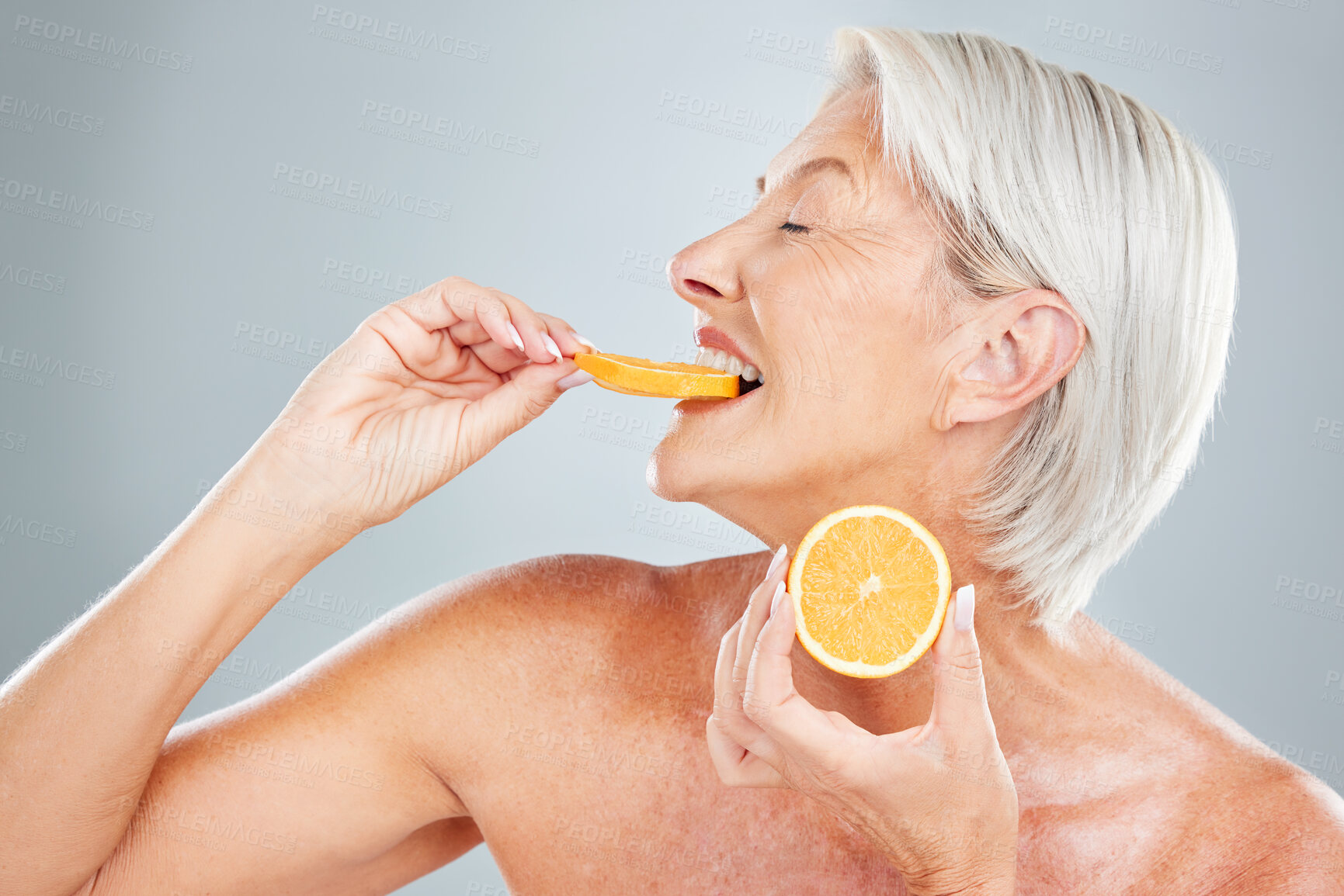 Buy stock photo Beauty, orange and eating with a mature woman biting into a fruit slice in studio on a gray background. Food, wellness and natural care with a senior female posing to promote healthy eating or diet