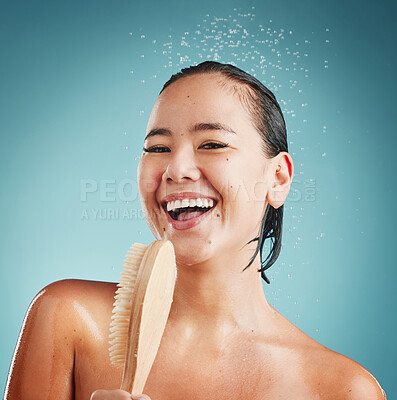 Buy stock photo Portrait, bath brush and woman in a shower for cleaning, wellness and skin exfoliate, beauty and grooming in a studio. Skincare, water splash and face of asian model washing, relax on blue background