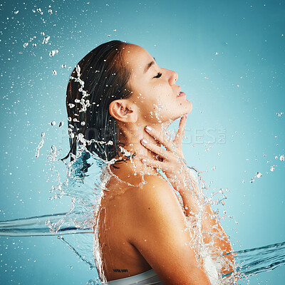 Buy stock photo Water, hydration and cleansing with a woman in studio on a blue background with a liquid splash for hygiene. Relax, luxury and wellness with an attractive young female washing in a bathroom or shower