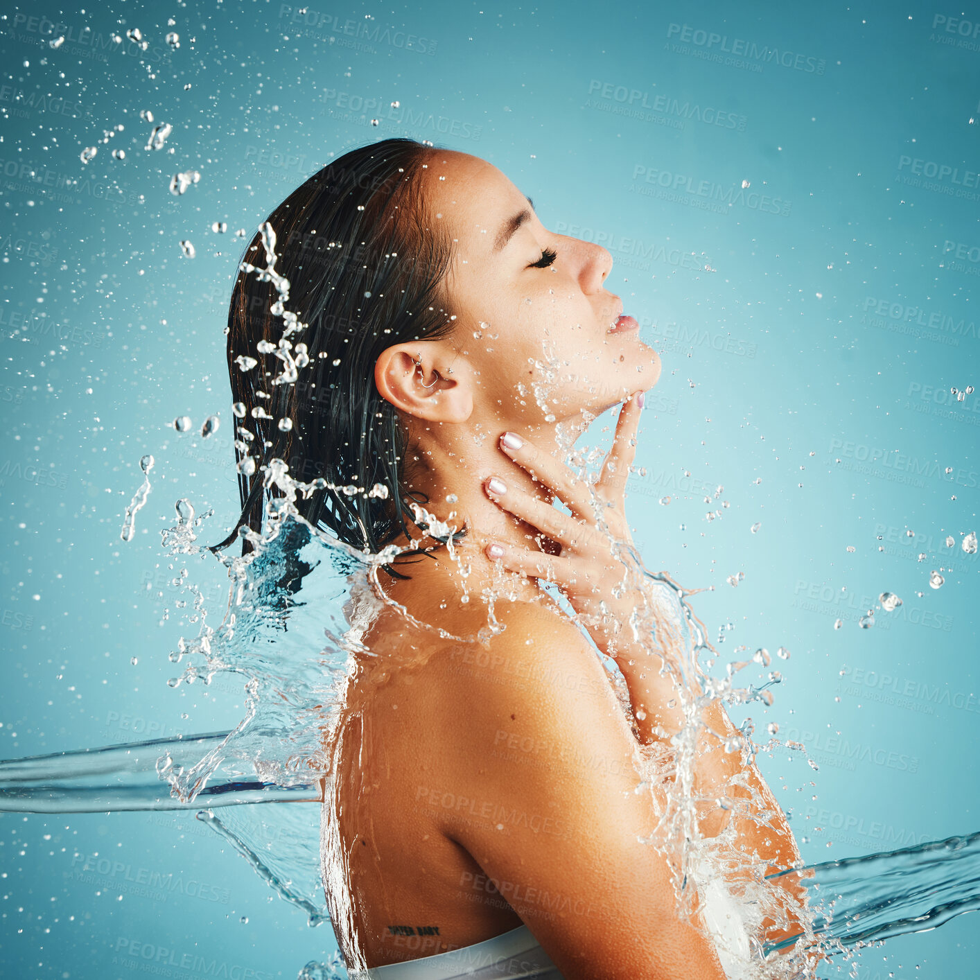 Buy stock photo Water, hydration and cleansing with a woman in studio on a blue background with a liquid splash for hygiene. Relax, luxury and wellness with an attractive young female washing in a bathroom or shower