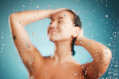 Buy stock photo Glass, shower and hygiene with a woman cleaning or washing her body in studio on a blue background. Water, relax and wellness with a female in the bathroom to clean, wash or hydrate her skin