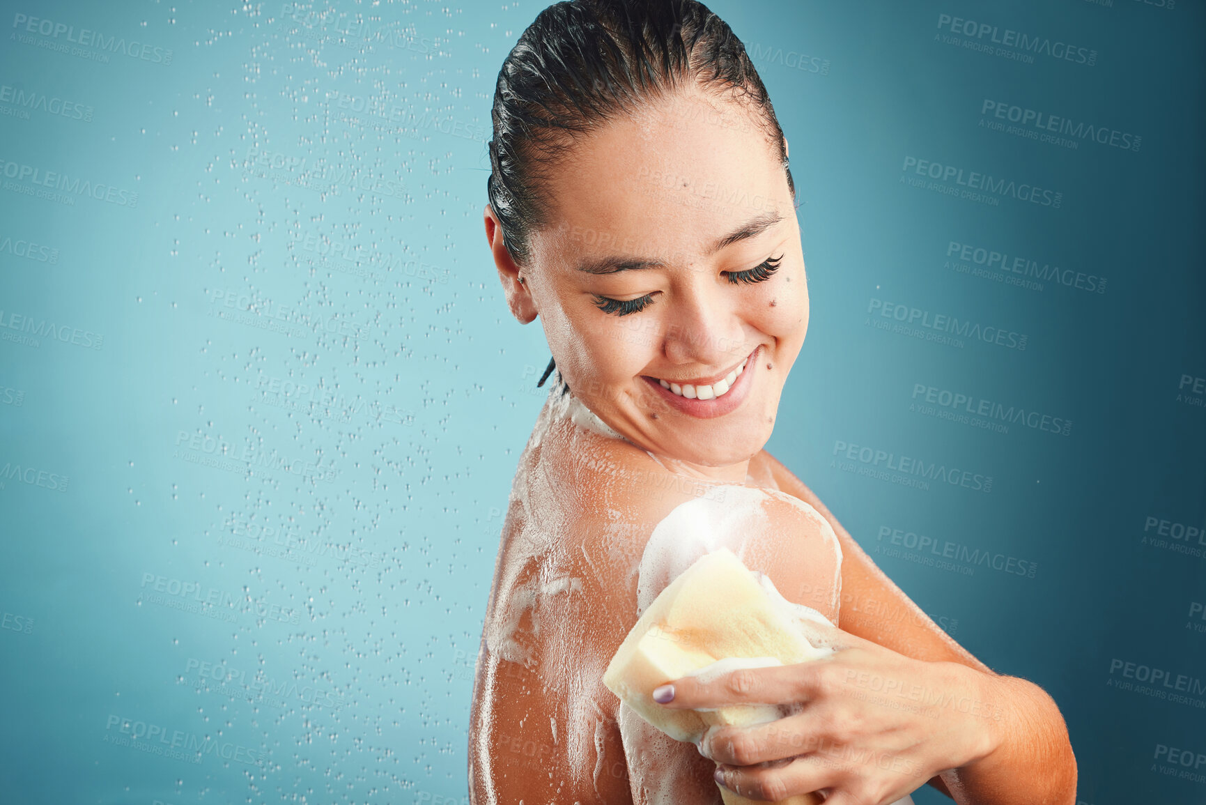 Buy stock photo Shower, sponge and soap with a woman cleaning her body in studio on a blue background with mockup. Water, hand and wellness with an attractive young female washing in the bathroom for hygiene