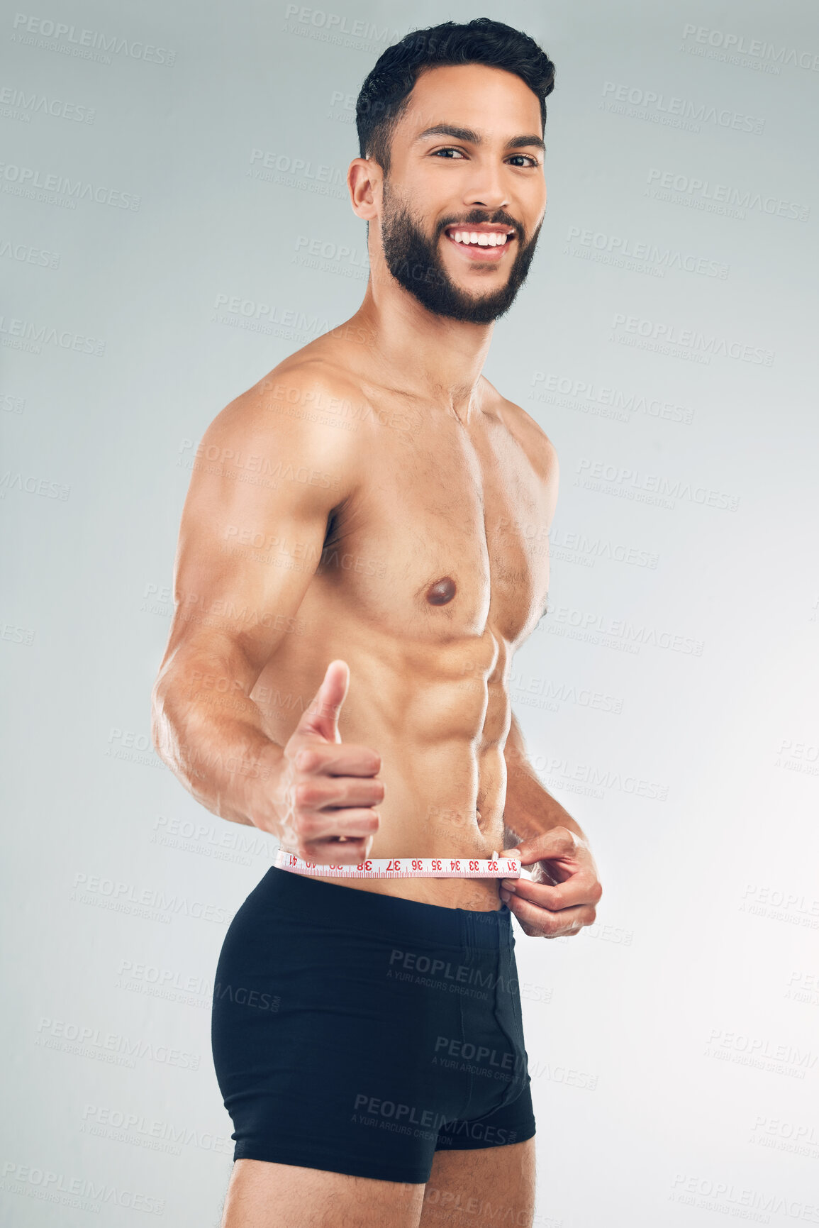 Buy stock photo Body, waist and thumbs up with a man model in studio on a gray background to promote weightloss or exercise. Portrait, fitness and diet with a young male measuring for health, success or motivation