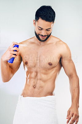 Buy stock photo Spray, clean and body of a man with deodorant after a shower against a grey studio background. Wellness, happy and young model with a smile for a fragrance product, health and happiness for hygiene