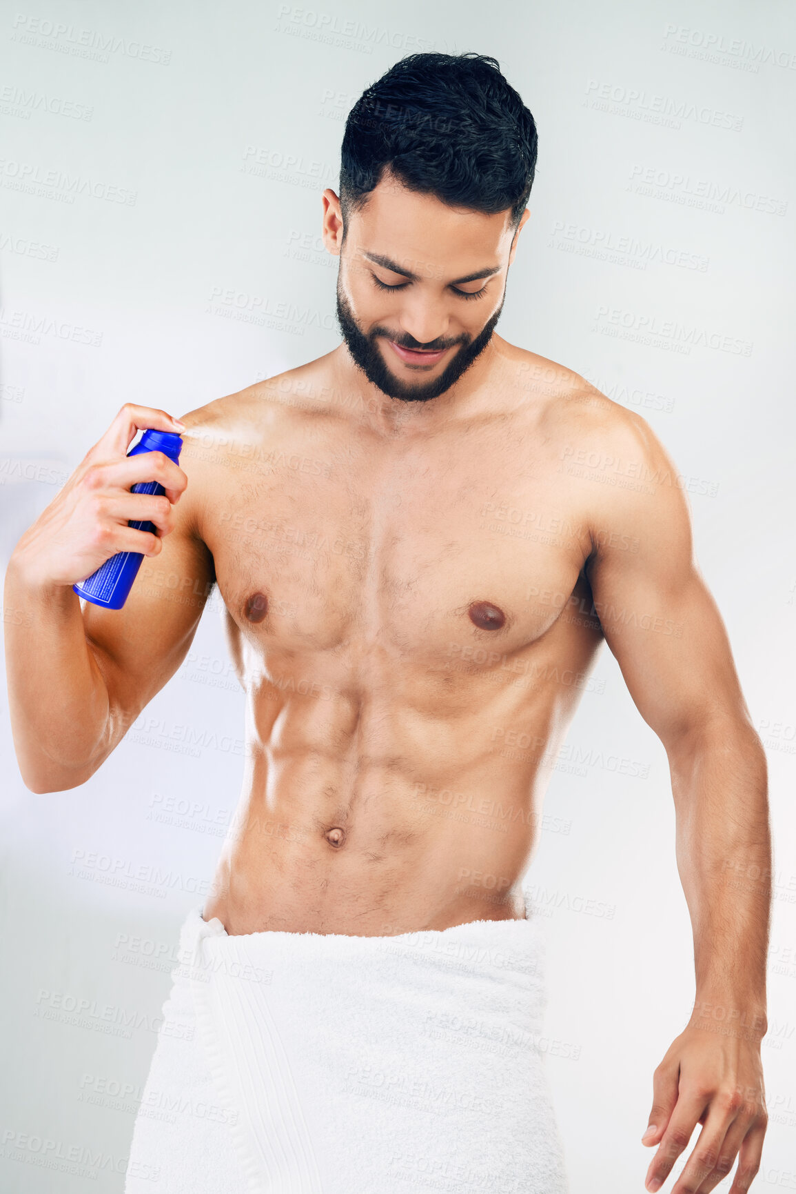 Buy stock photo Spray, clean and body of a man with deodorant after a shower against a grey studio background. Wellness, happy and young model with a smile for a fragrance product, health and happiness for hygiene