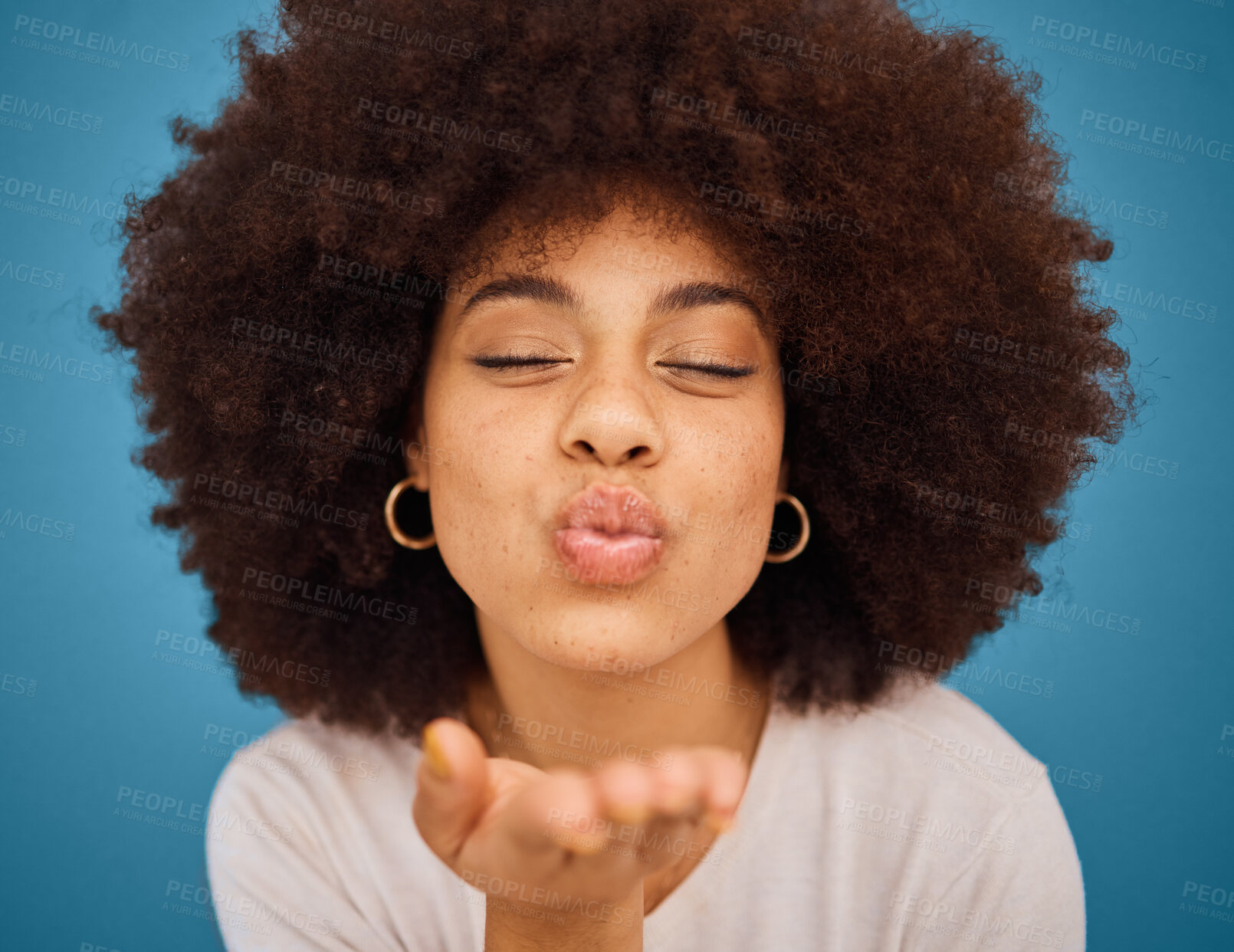 Buy stock photo Care, love and black woman blowing kiss with a smile, afro hair and hand against a blue studio background. Happy, beauty and face of a cool, African and young girl model with affection and happiness 