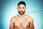 Splash, water and portrait of a man cleaning body with hydration against a blue studio background. Sexy, wellness and face of a model washing for hygiene, grooming and health with liquid on skin