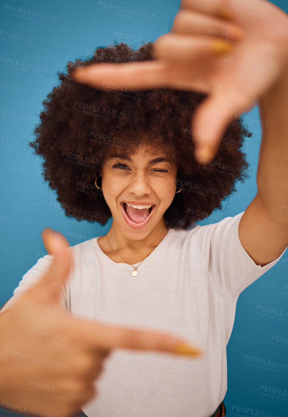 Buy stock photo Black woman, hand frame afro and studio beauty with wink, smile and comic pose by blue background. African model woman, sign hands and funny portrait with happy face, photography and play by backdrop