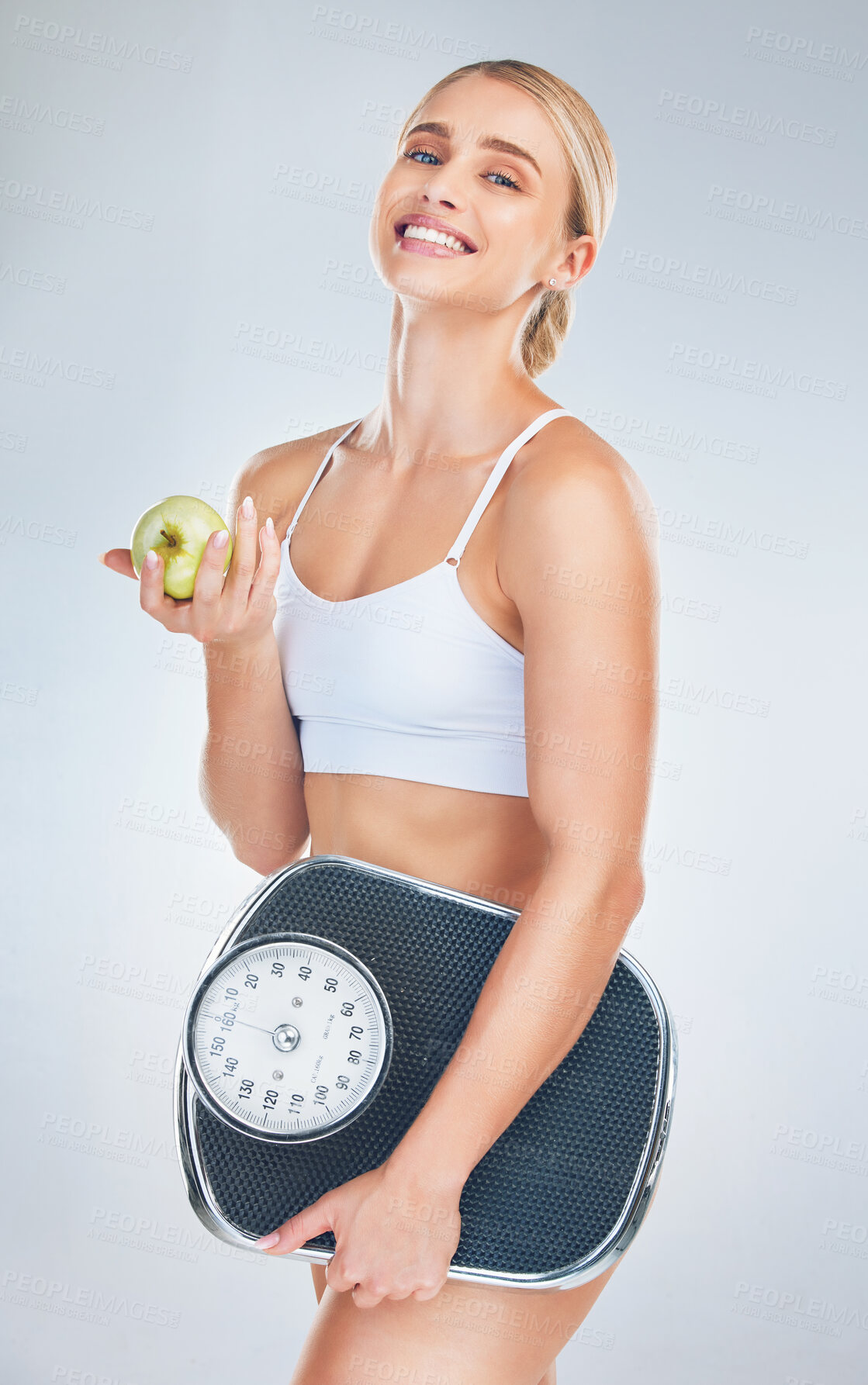 Buy stock photo Health, lose weight and woman with an apple and scale for body goal, motivation and nutrition against a grey studio background. Food, happy and portrait of athlete model with smile for fruit and diet