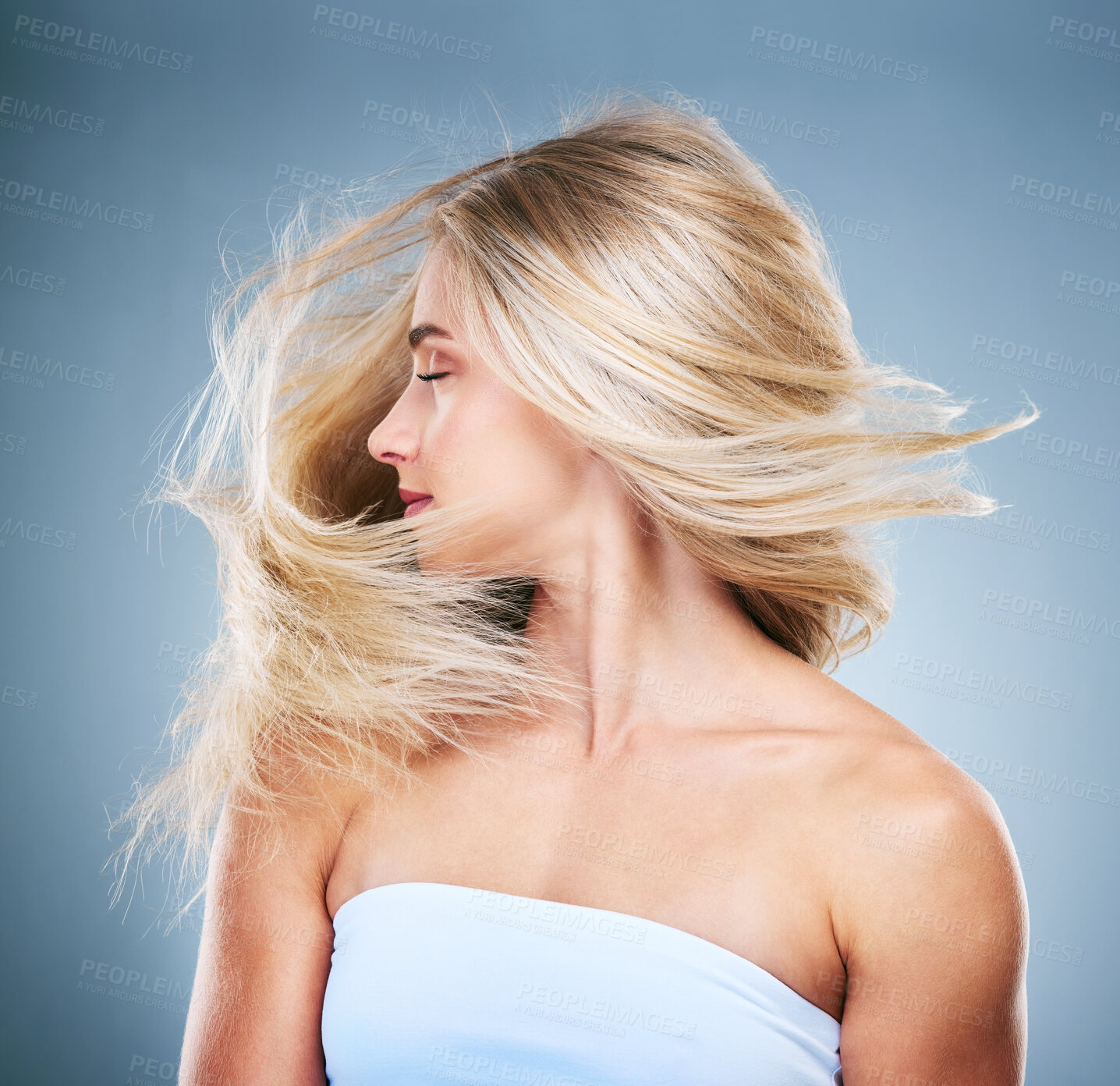 Buy stock photo Woman, hair and blonde with wind in studio for hair care, cosmetics and beauty against blue background. Model, girl and healthy hair from side by blue backdrop with shake, turn and cosmetic fashion