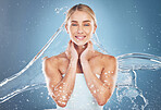 Water, hydration and portrait of a woman with a splash for skincare, wellness and beauty against a blue studio background. Spa, cleaning and portrait of a happy model with liquid to clean body