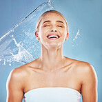 Water, beauty and cleaning with a model woman in studio on a blue background for hydration in a splash. Shower, skincare and wellness with an attractive young female wet for luxury or hygiene