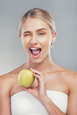 Buy stock photo Woman, health and wink portrait with apple for fiber diet, nutrition and wellness lifestyle. Fruit, healthy and digestion dieting marketing with happy model girl on gray studio background.